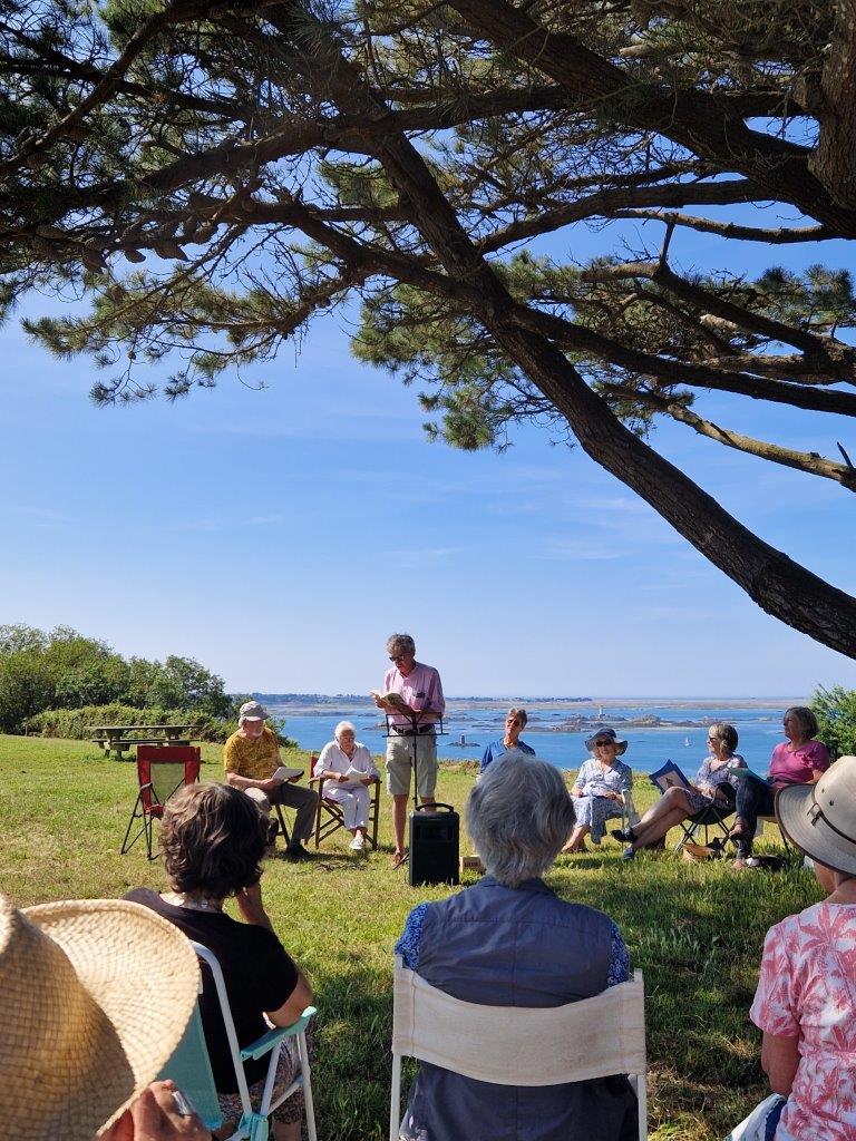 Des personnes écoutent une lecture en plein air devant la mer.