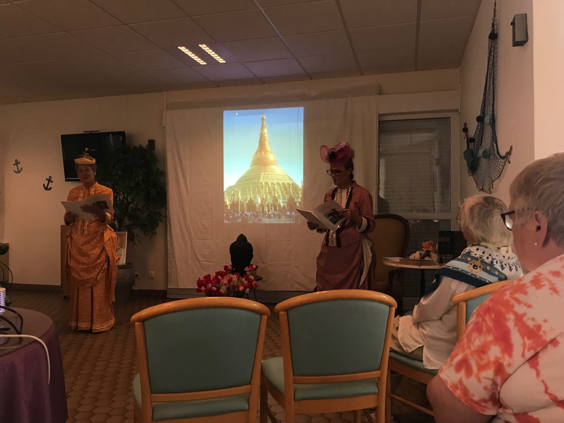 Deux femmes en costume lisent des textes avec une projection au mur.